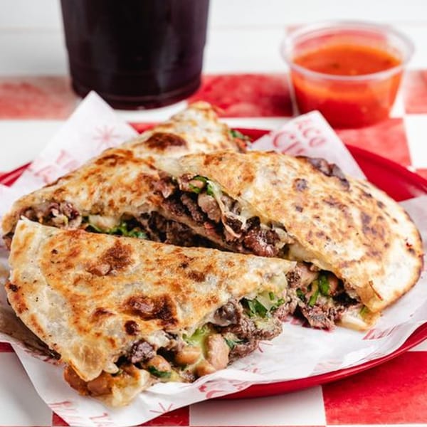 Three large, golden-brown quesadillas filled with meat and cheese, served with salsa and a drink.