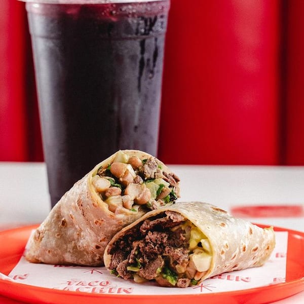 Two burritos with meat and beans on a red plate with a dark drink in the background.