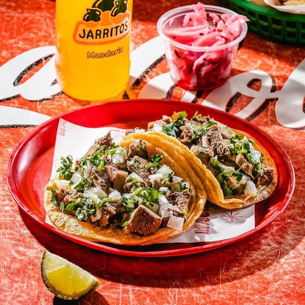 Two carne asada tacos with onion and cilantro, a Jarritos soda, and pickled onions.